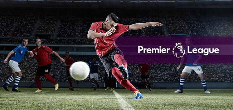 A football player in a red jersey taking a powerful shot on goal during a Premier League match, with the Premier League logo overlayed on the image