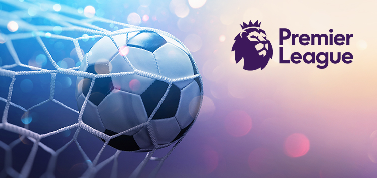 The image shows a football hitting the back of a net with a blurred, colourful background. The Premier League logo features a stylised lion's head with a crown in the top right corner. The overall theme suggests excitement and anticipation surrounding a Premier League weekend.