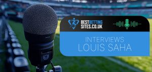 Image of a microphone set up near the sidelines of a football stadium with the BestBettingSites.co.uk logo and the text "Interviews Louis Saha" overlaid, indicating an interview with the former footballer.